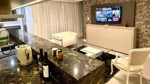 A modern kitchen with a marble countertop, a built-in oven, and a TV mounted on the wall displaying a drama channel. - Be Haus Temporary Apartments (San Luis)