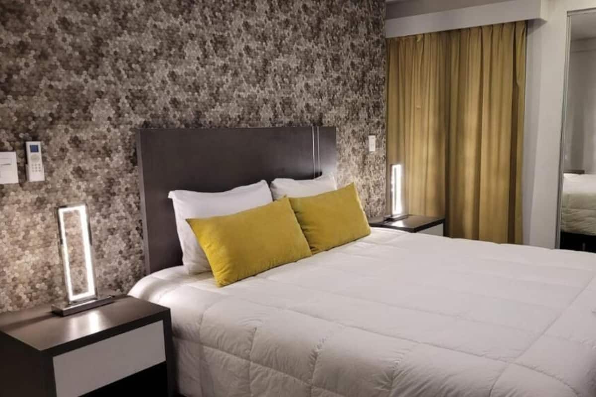 A hotel room with a large bed, a headboard, two bedside tables, and a mirror.