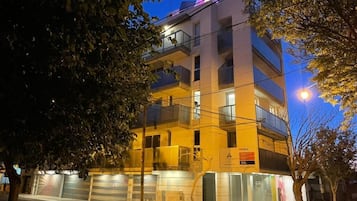 A multi-story building with balconies, a visible sign, and a street view at night.