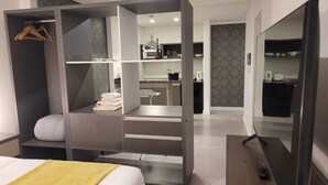 A modern hotel room with a walk-in closet, a kitchenette, and a large mirror. - Be Haus Temporary Apartments (San Luis)