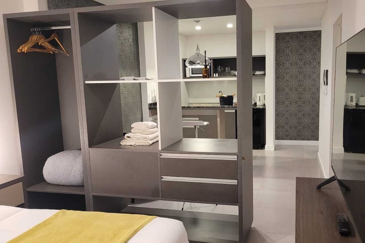 A modern hotel room with a walk-in closet, a kitchenette, and a large mirror.
