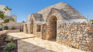 Un edificio de piedra con techo de tejas y puertas arqueadas, rodeado de un muro de piedra y un camino empedrado.