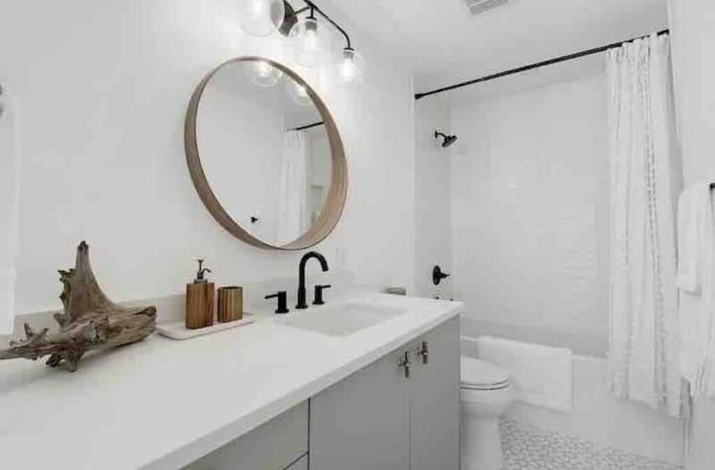 Un baño moderno con un lavabo blanco, un espejo redondo y una cortina de ducha.