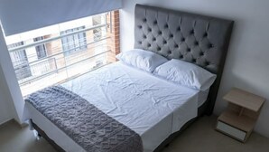 A bedroom with a large bed, a grey headboard, and a window with a view of buildings. - Apartamento en Pitalito (Pitalito)