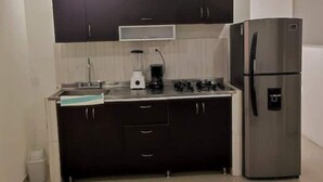 A compact kitchen with dark cabinets, a stainless steel refrigerator, a gas stove, and a coffee maker. - Apartamento en Pitalito (Pitalito)