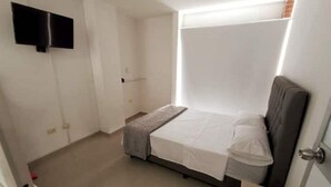 A small, single-bed room with a grey headboard, a bedside table, and a flat-screen TV mounted on the wall. - Apartamento en Pitalito (Pitalito)