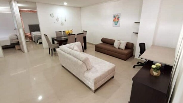 A modern living room with a sofa, a dining table with chairs, and a small desk with a lamp. - Apartamento en Pitalito (Pitalito)