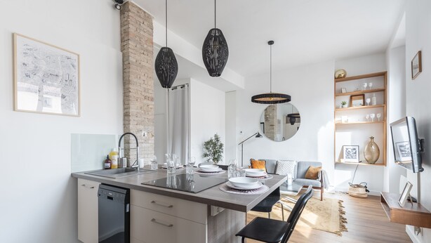 A modern kitchen with a dishwasher, a dining area with a bench, and a living space with a sofa and a TV.