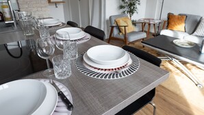 A dining table set with plates, glasses, and cutlery, a sofa, a lamp, and a plant in a modern living room.