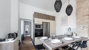 A modern kitchen with a dining area, featuring a large island, black chairs, and a brick wall.