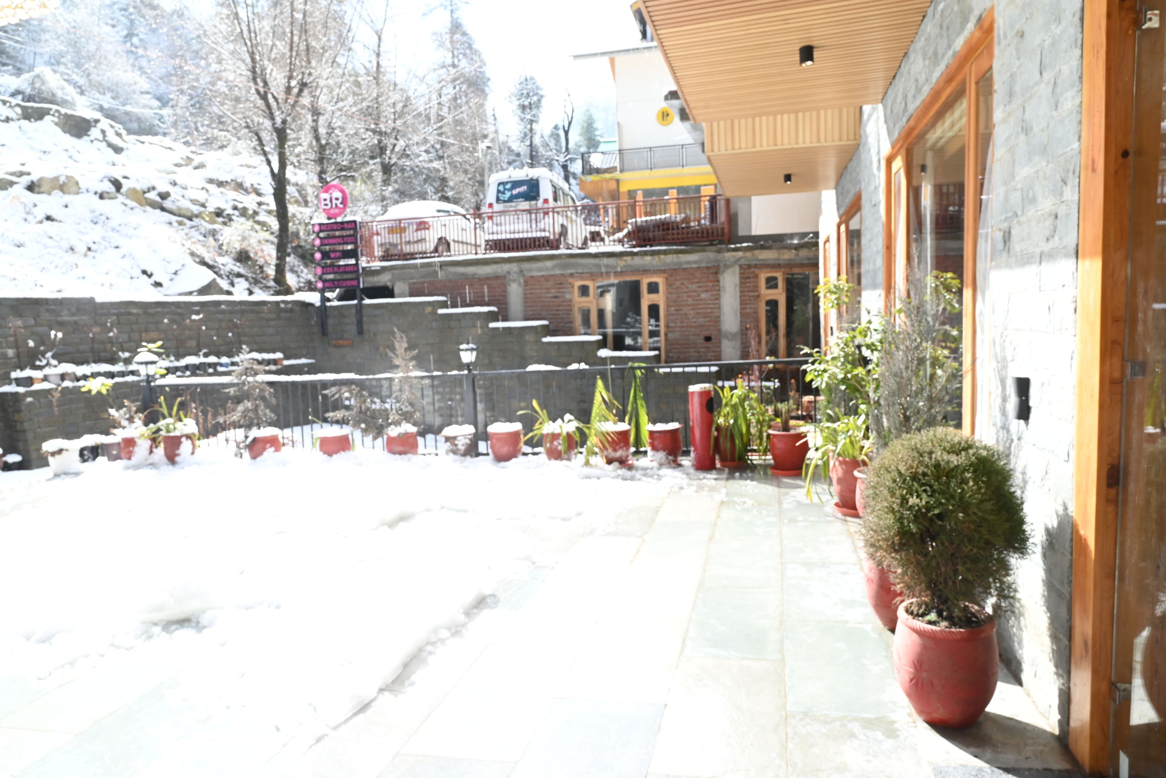 Un edificio con fachada de piedra, plantas en macetas y suelo cubierto de nieve.