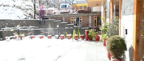 Un edificio con fachada de piedra, plantas en macetas y suelo cubierto de nieve.