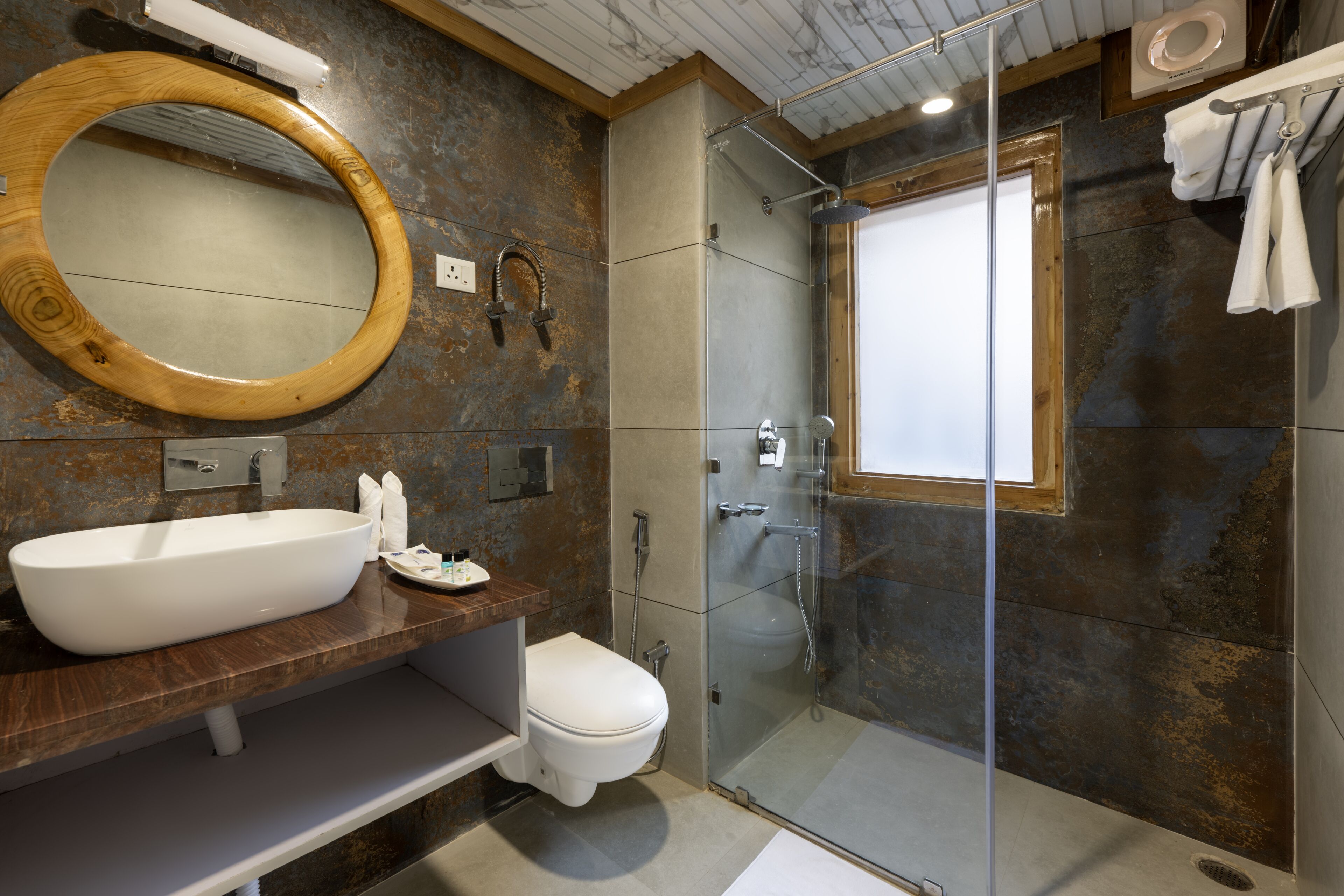 Une salle de bain moderne avec un grand miroir ovale, un lavabo blanc, des toilettes et une douche séparée par une paroi de verre.