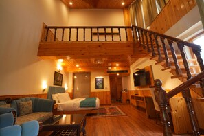 A spacious living area with a wooden staircase, a sofa, a coffee table, and a television. - Bradhi - Riverside Resort Jibhi (Banjar)