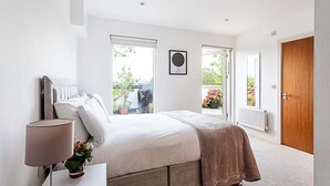 Ein Schlafzimmer mit Bett, Nachttisch, Lampe und einem Fenster mit Blick ins Freie.