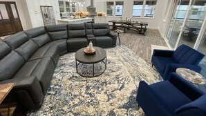 Ein geräumiges Wohnzimmer mit einem großen Ecksofa, einem runden Couchtisch und einem blauen Sessel.