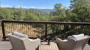 Eine Holzterrasse mit Korbmöbeln und einem Tisch, mit Blick auf eine Berglandschaft.