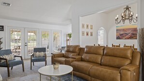 Een woonkamer met een bruine leren bank, twee fauteuils, een salontafel en een groot raam met uitzicht op een canyon.