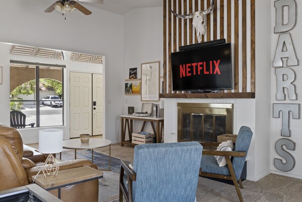 A modern living room with a fireplace, a television displaying 'NETFLIX', and a large 'DARTS' sign on the wall. - PRIVATE Launch & Beach, 3 Bd, 2 Ba - "The Bullhead Boho" (Bullhead City)