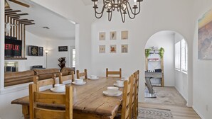 Een eetruimte met een houten tafel gedekt voor zes personen, omringd door houten stoelen. Een kroonluchter hangt erboven en de muren zijn versierd met kunstwerken in lijsten.