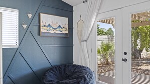 Een kamer met een donkerblauwe accentmuur, een relaxfauteuil, een kunstwerk in een lijst en een uitzicht door een glazen deur op een buitenruimte met planten.