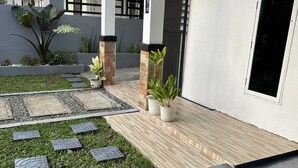 A modern building with a covered outdoor area featuring a paved walkway, potted plants, and a grassy section. - Private townhouse, located in a private subdivision with guards on site.  (San Pablo City)