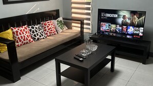 A modern living room with a sofa, coffee table, and a TV displaying a show. - Private townhouse, located in a private subdivision with guards on site.  (San Pablo City)