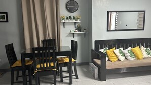 A dining area with a table and chairs, a sofa with cushions, a clock, and a shelf with plants. - Private townhouse, located in a private subdivision with guards on site.  (San Pablo City)