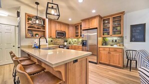 Una cocina moderna con armarios de madera, una isla central con taburetes de bar, electrodomésticos de acero inoxidable y un letrero de pizarra.
