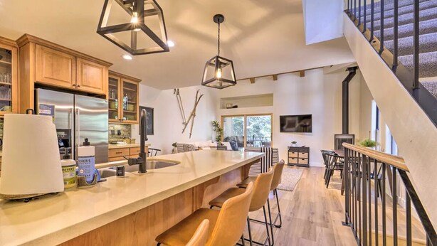 Una cocina moderna con una isla central, taburetes de bar y una escalera que lleva a un nivel superior.