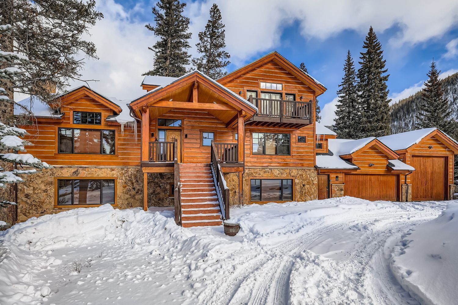 A multi-story log cabin with a stone foundation, a balcony, and a staircase leading to the upper levels.