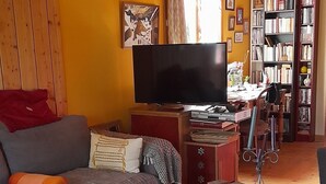 Una sala de estar acogedora con techo de madera, un sofá, una mesa de centro, un televisor y una estantería llena de libros.
