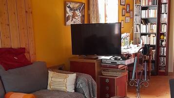 Una sala de estar acogedora con techo de madera, un sofá, una mesa de centro, un televisor y una estantería llena de libros.