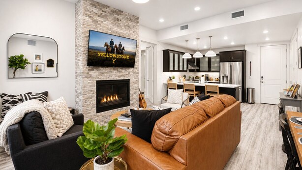Una sala de estar moderna con chimenea, un televisor montado y un comedor con cocina al fondo.