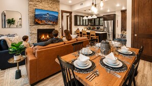 Una sala de estar moderna con chimenea, un comedor para seis personas y una cocina al fondo.