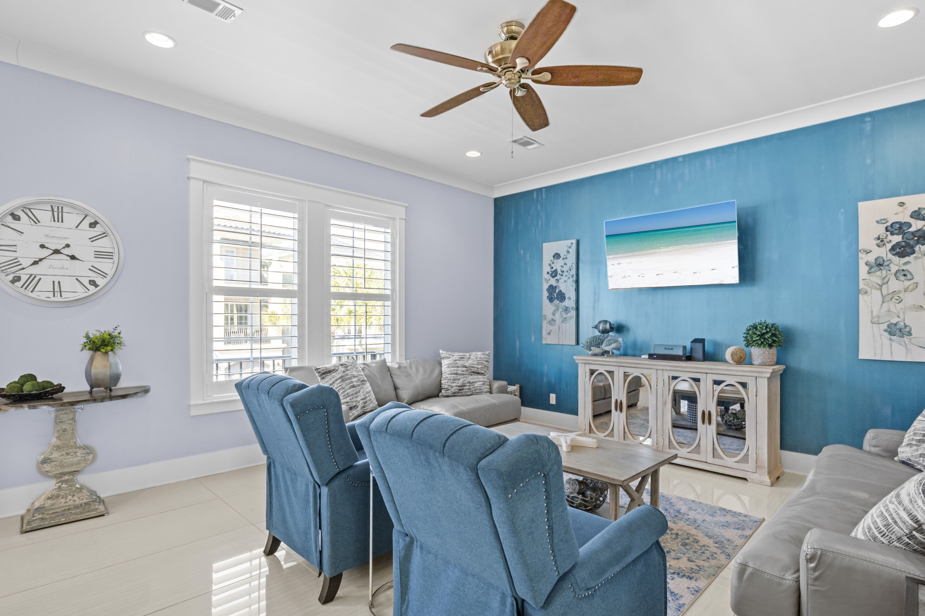 Un salon avec un ventilateur de plafond, une horloge, un canapé et une table basse.