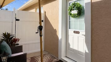 A covered patio area with a wicker sofa, a small table with a lamp, and a welcome wreath on the door.