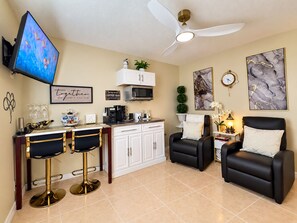 A modern living room with a TV, a coffee bar, two black leather chairs, a sofa, and a ceiling fan.