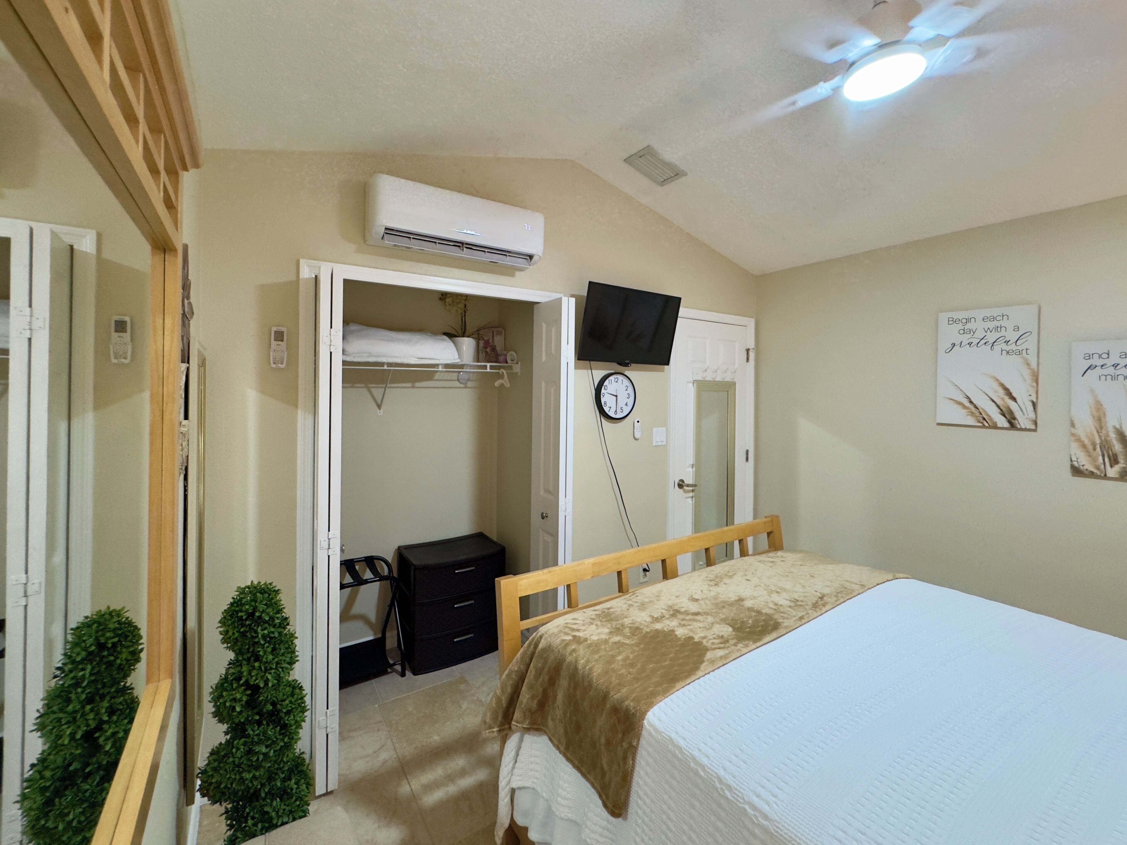 Une chambre à coucher avec un lit, une armoire, une télévision et une horloge au mur.