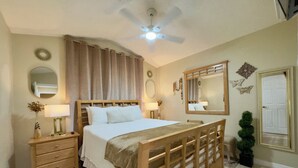 Ein Schlafzimmer mit einem hölzernen Bett, zwei Nachttischen, einem Deckenventilator, einem Spiegel und einer Tür.