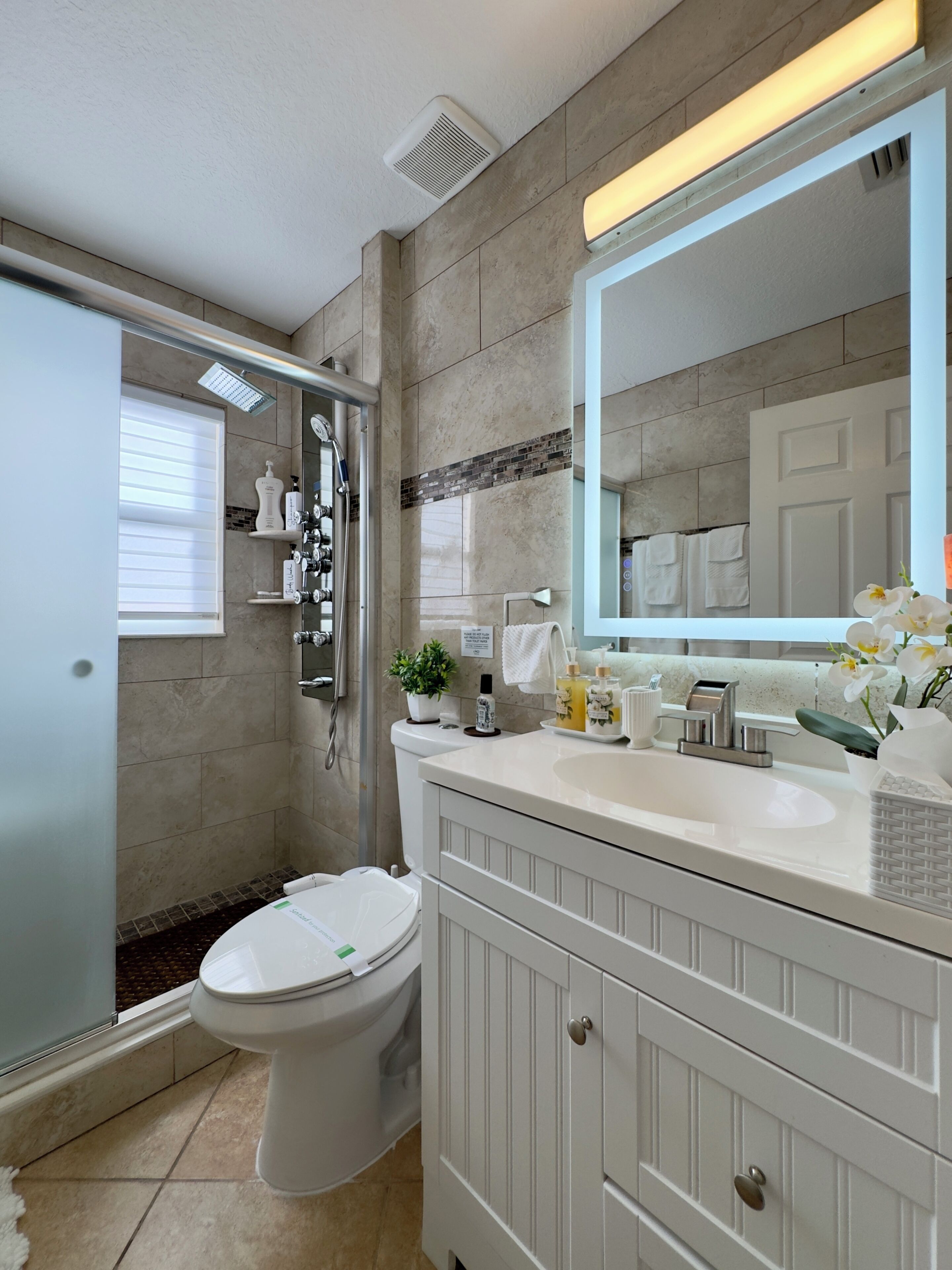 Une salle de bain moderne équipée d’une douche, de toilettes, d’un meuble-lavabo et d’un grand miroir.