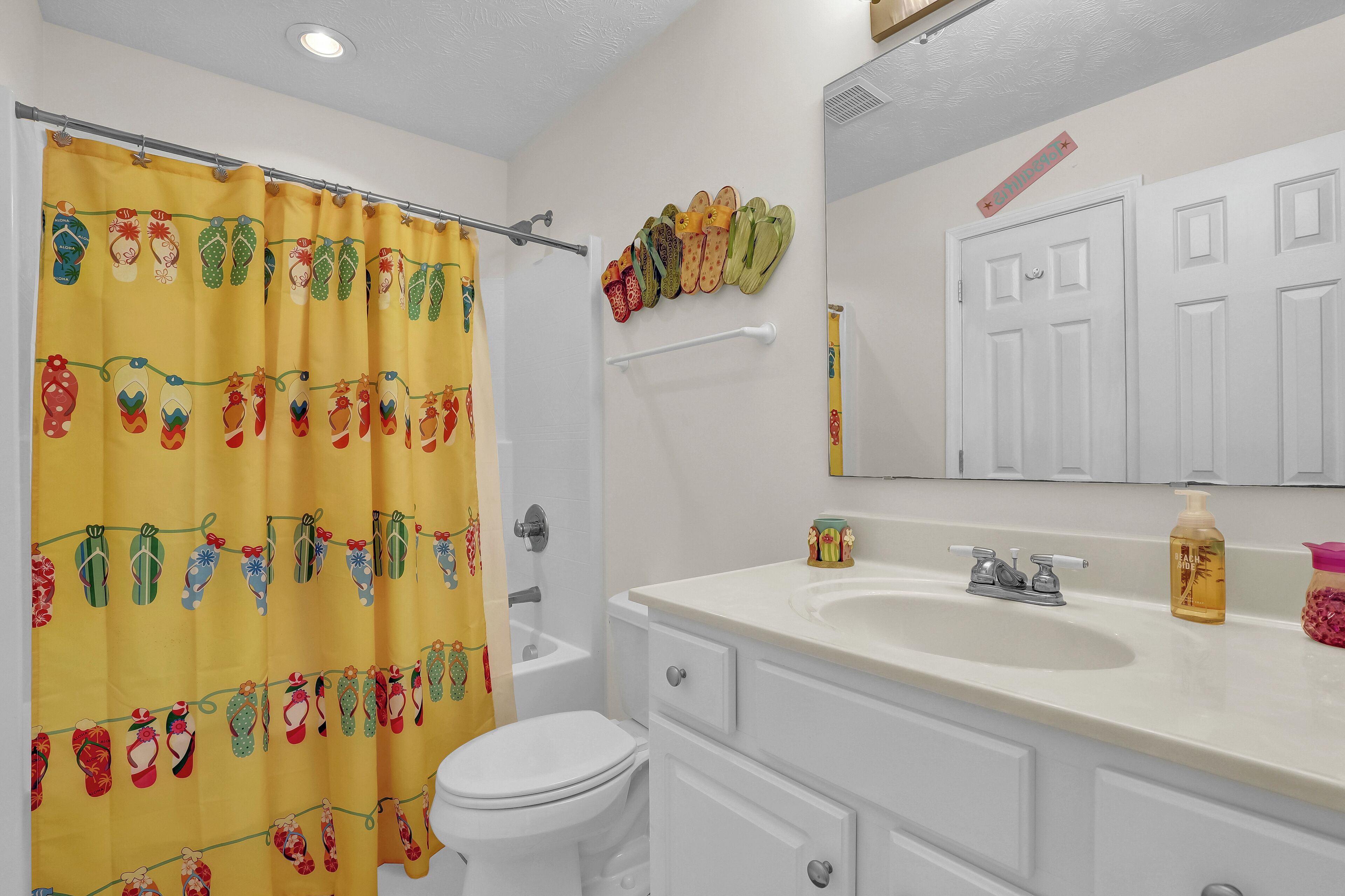 A bathroom with a yellow shower curtain, a toilet, a sink, and a mirror.