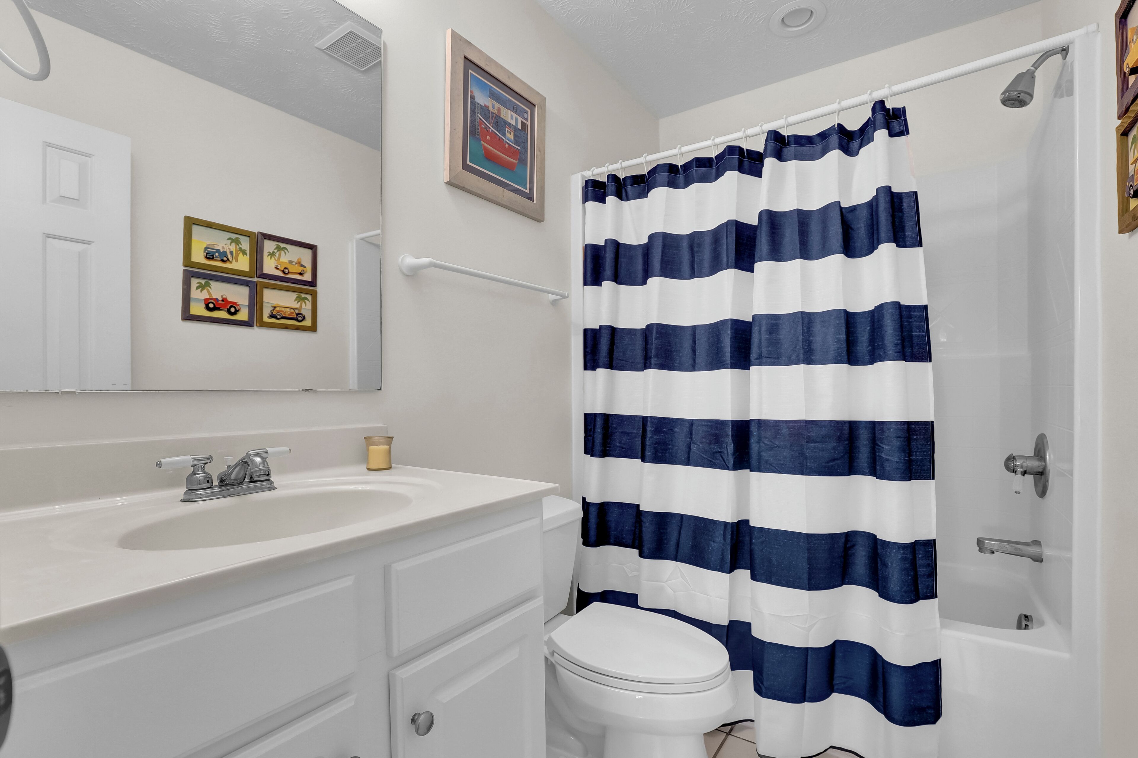 Un baño con un lavamanos blanco, un inodoro y una cortina de ducha con rayas azules y blancas.