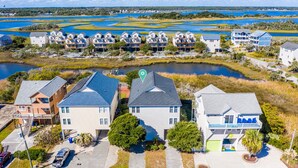 A residential area with houses near a body of water, featuring a mix of single and multi-story buildings, a visible green marker, and a clear sky. - Sunset Horizon | Private Fenced-in Backyard | Surf City! (surf ctiy)