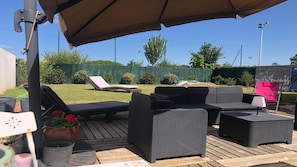 An outdoor patio area with wicker furniture, a table, and a chair. - Commentaire Sous peu (L'Houmeau)