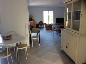A spacious living area with a dining table, chairs, a sofa, and a television. - Commentaire Sous peu (L'Houmeau)