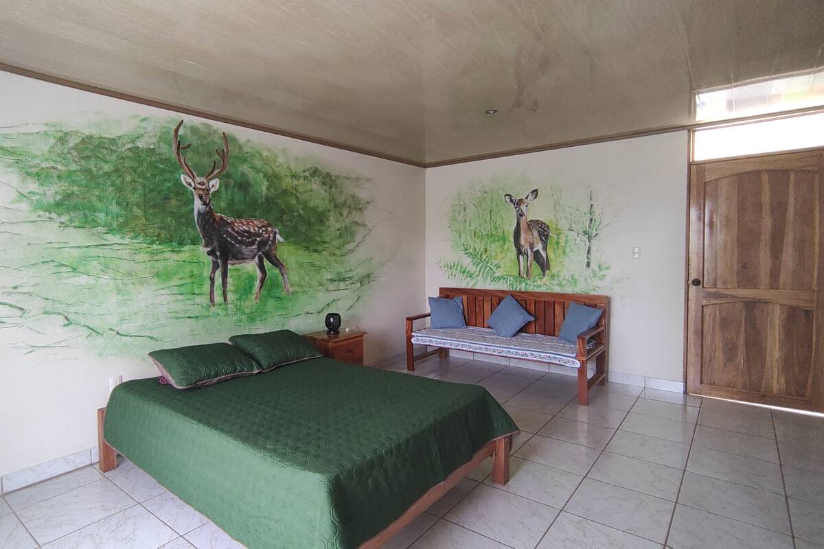 Une chambre à coucher avec un lit, un banc et deux œuvres d’art murales représentant des cerfs.