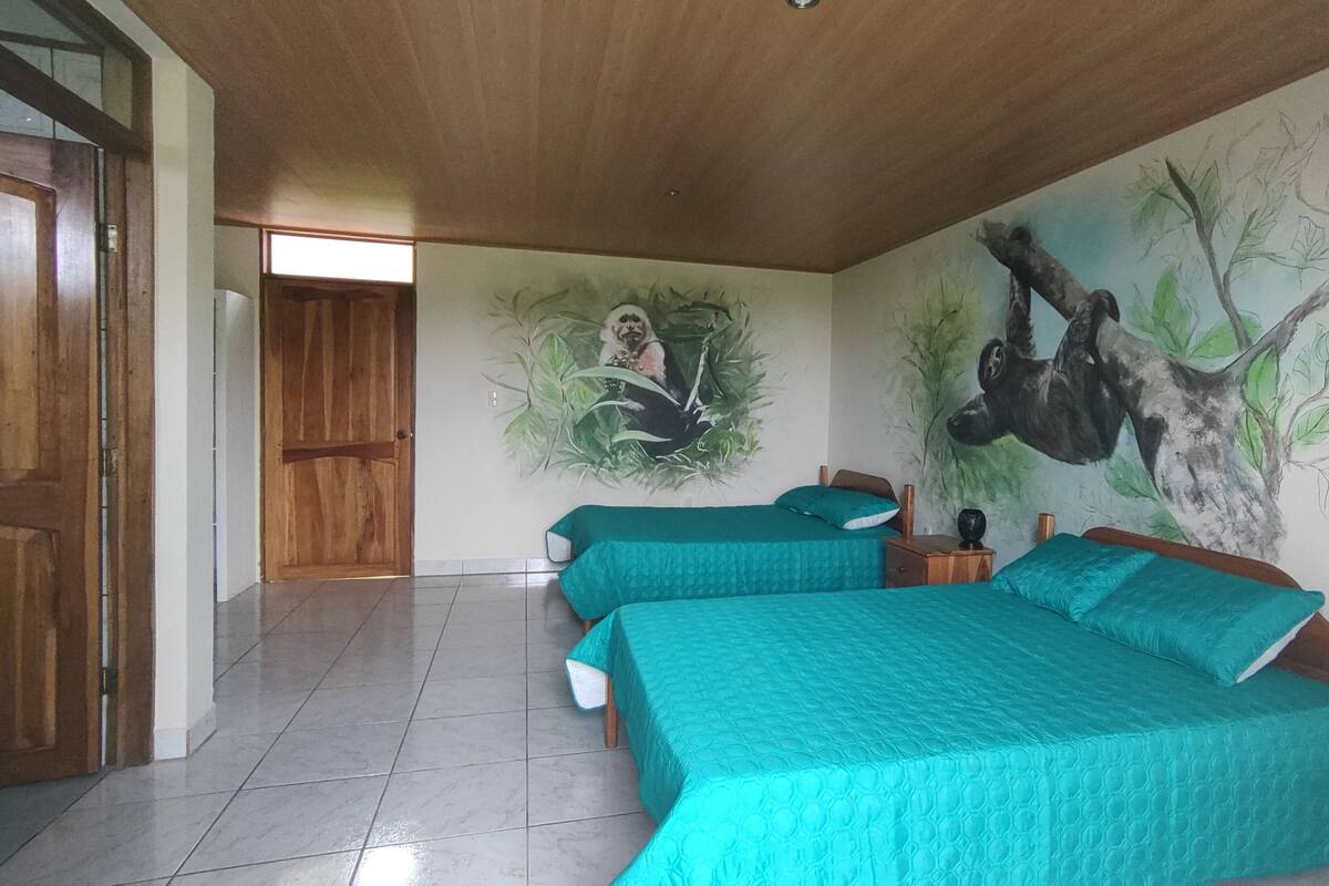 Une chambre avec deux lits, une porte en bois, un sol carrelé et une fresque murale.