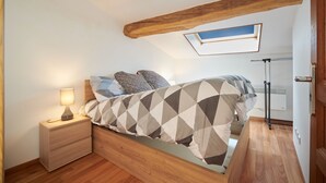 Un dormitorio con una cama, una mesita de noche, una lámpara, techo de madera y un tragaluz.