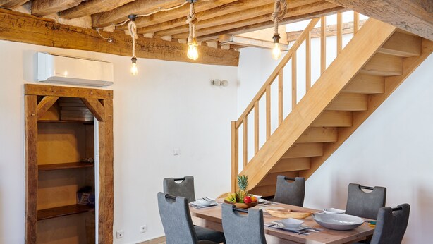 Un comedor con una mesa de madera, sillas y una escalera.